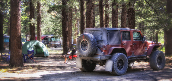 A Jeep Wrangler parked beside a green dome tent on a pine-shaded overland site at Mammoth Mountain RV Park.