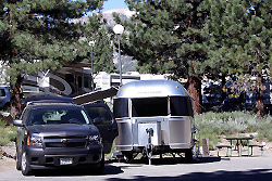 A silver Airstream trailer and pickup on a paved site at Mammoth Mountain RV Park with pines behind.