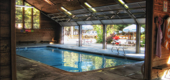 The indoor swimming pool at Mammoth Mountain RV Park, with a timber ceiling and glass doors opening onto the picnic area.